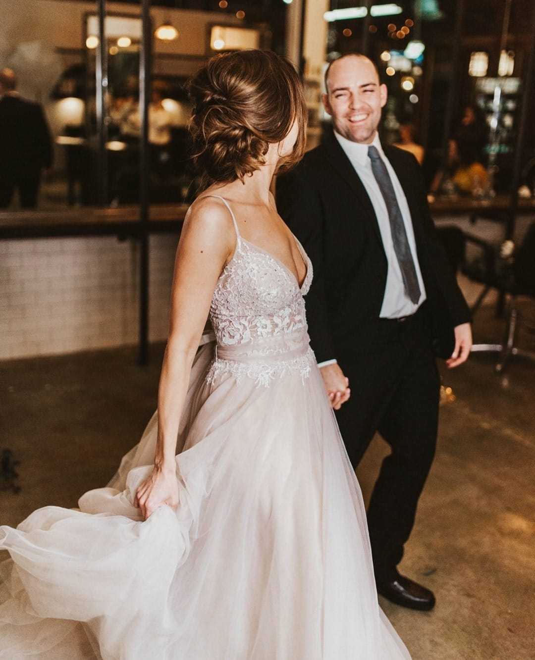 Bride and groom dancing at their wedding reception, smiling and holding hands.