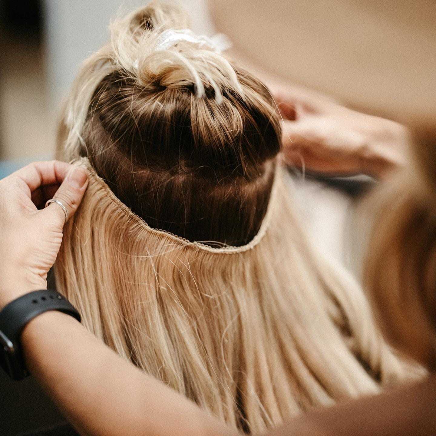Hair stylist attaching blonde hair extensions to a client's head.
