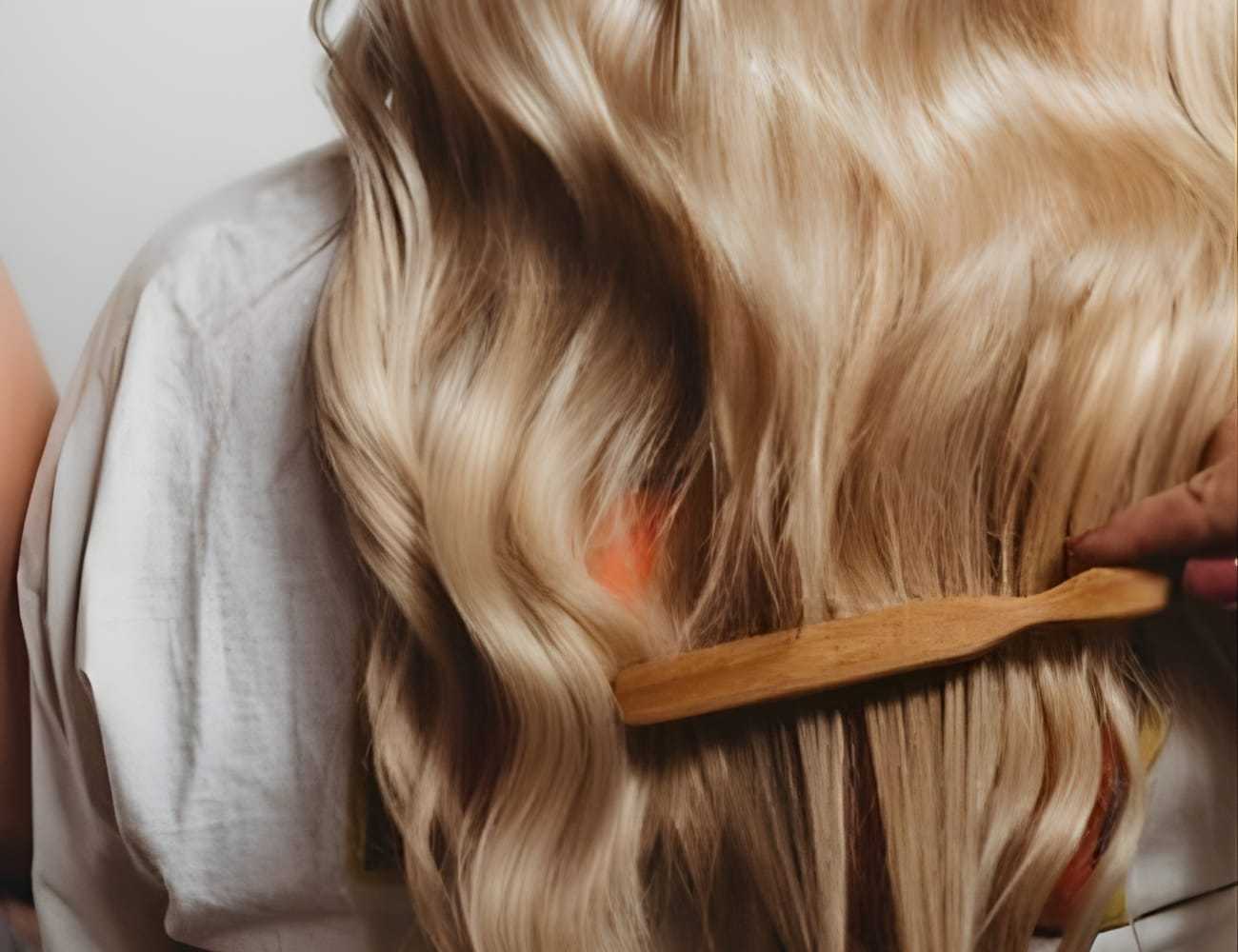 Brushing long, wavy blonde hair with a wooden comb.