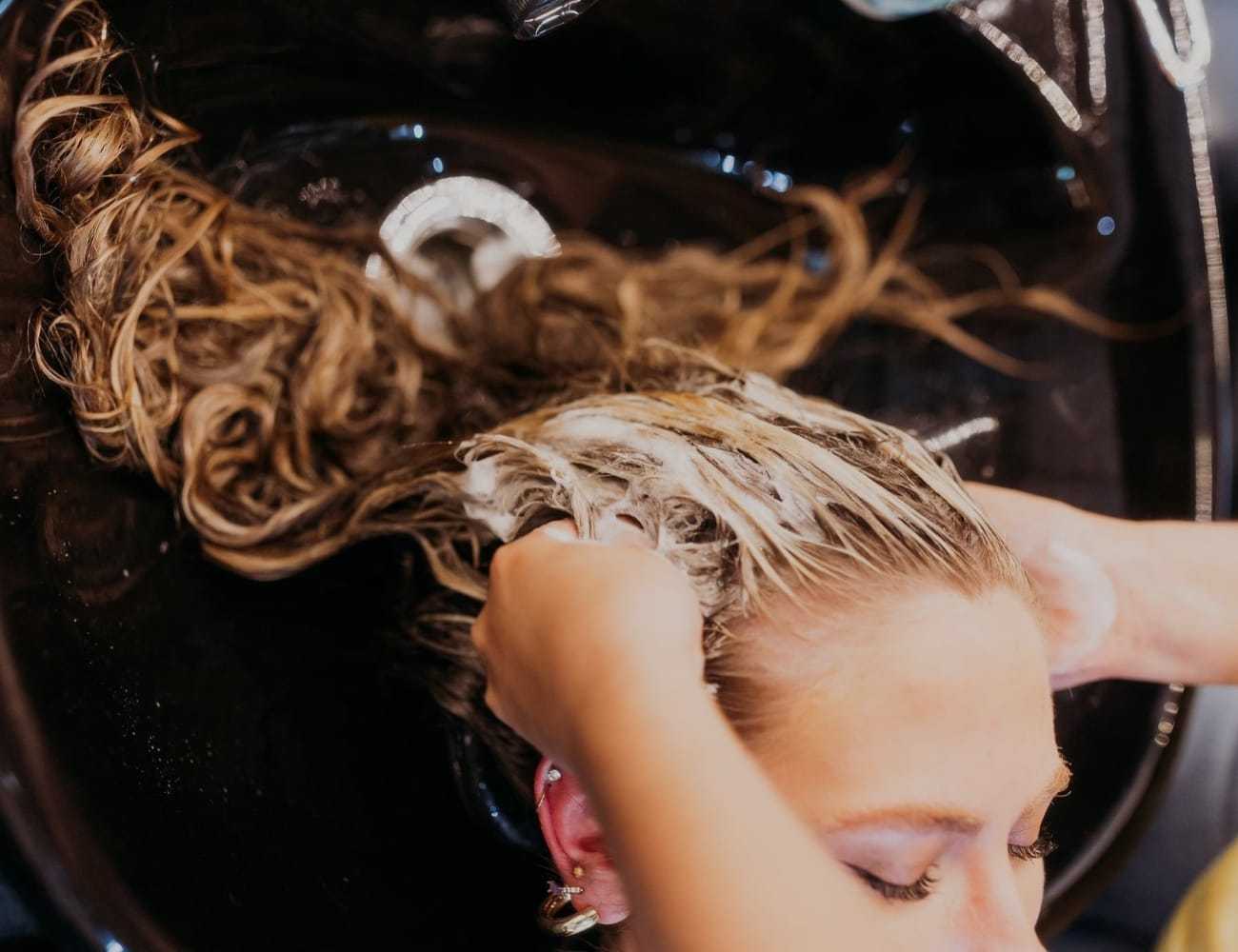 Hairdresser washing woman's hair in salon sink.